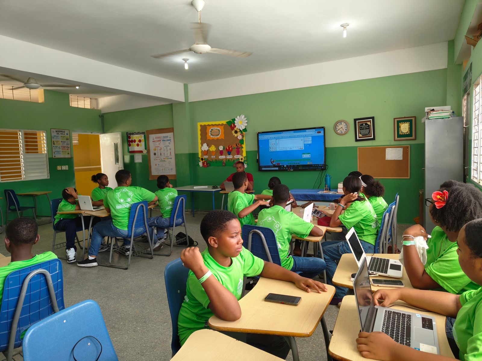 Students in green uniforms working on laptops in a modern classroom