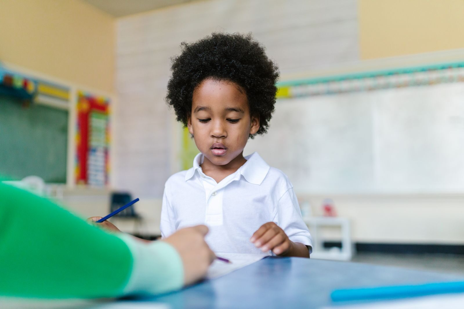 A young pupil in a white polo shirt working at his desk in a bright classroom